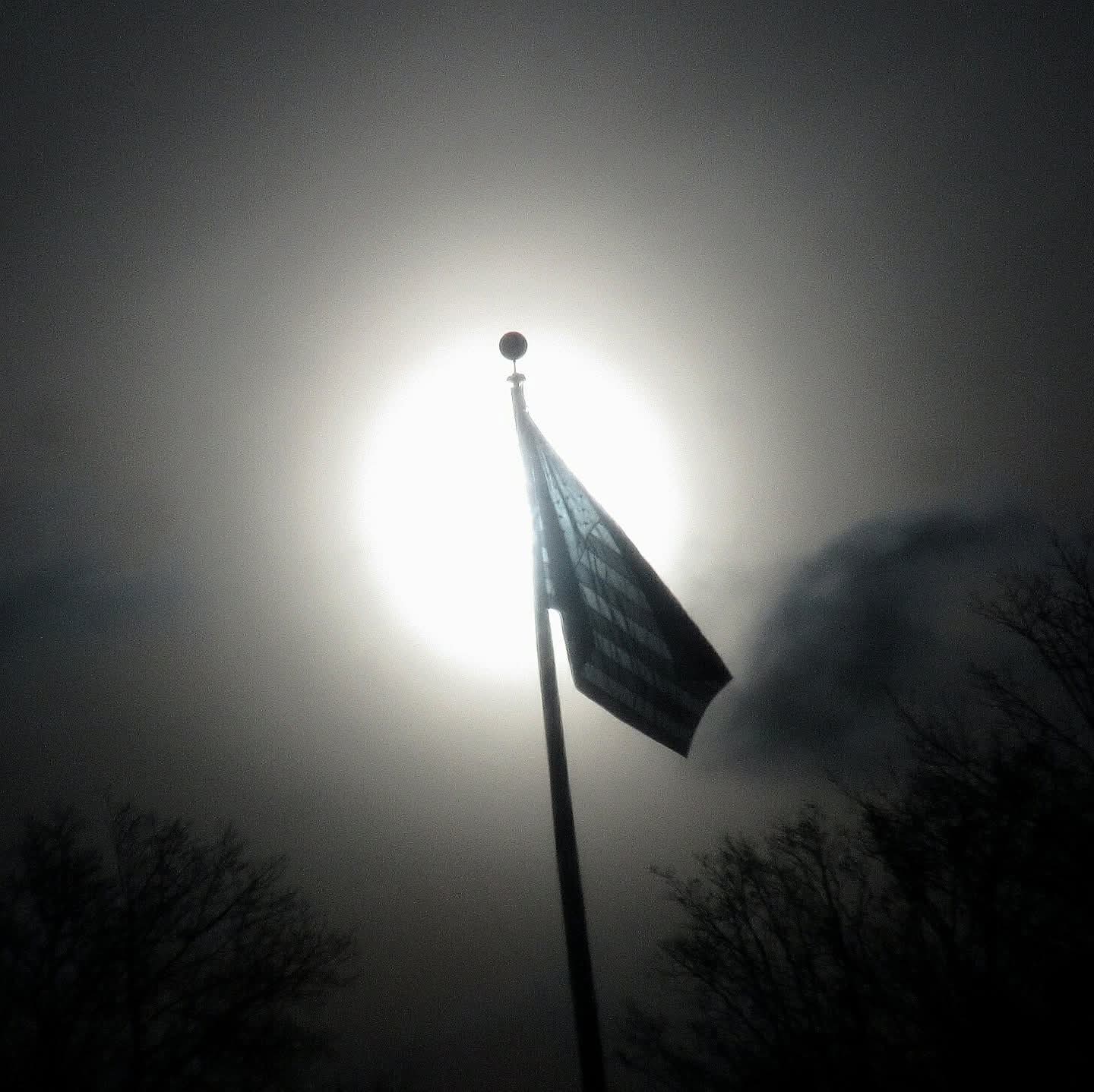 A flag and bright sun reflected in the window of a bus.