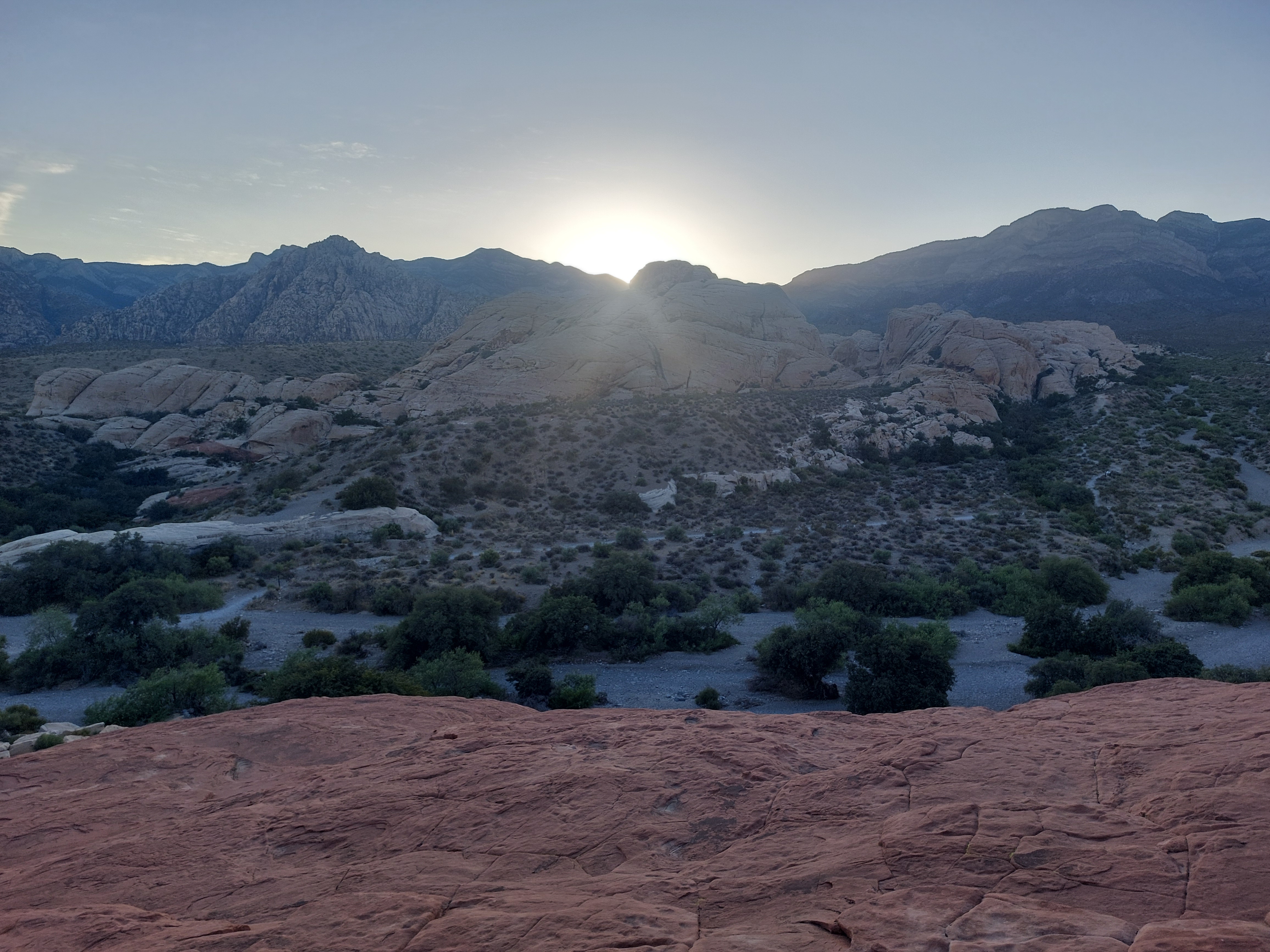 Sun setting over a broad red rock desert landscape.