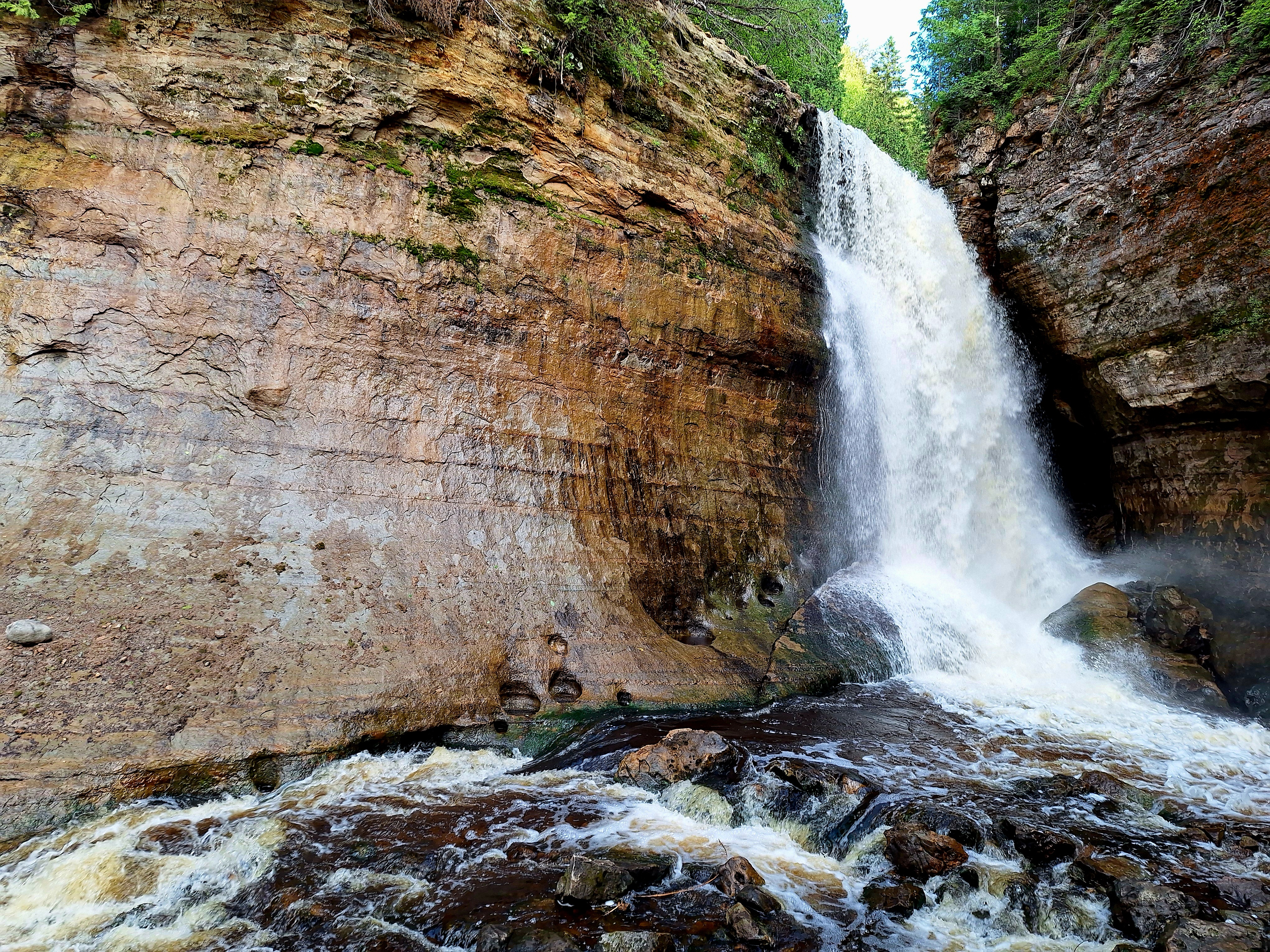 A waterfall dropping through layered rock into a foaming stream.